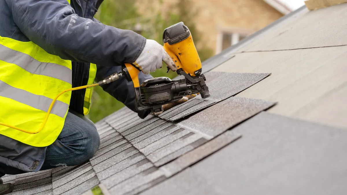 Arbeiter installieren mit Druckluftnagler Ziegel auf dem Dach eines neuen Hauses im Bau